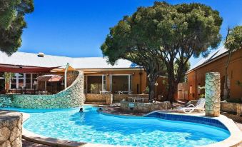 a beautiful swimming pool and surrounding area , with trees and buildings in the background , under a clear blue sky at Karma Rottnest