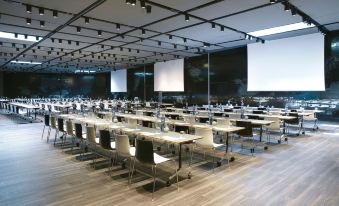 a large conference room with multiple rows of tables and chairs , white walls , and black screens at Renaissance Barcelona Fira Hotel