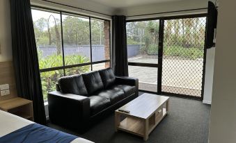 a modern living room with large windows , a black leather couch , and a wooden coffee table at Logan City Motor Inn