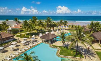 a tropical resort with a swimming pool , umbrellas , and palm trees near the ocean , under a clear blue sky at Hotel Village Porto de Galinhas