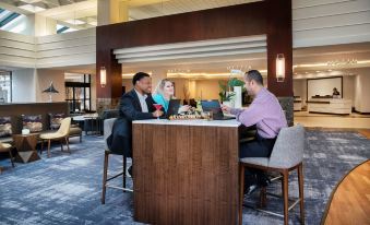 a group of people gathered around a wooden bar in a hotel lobby , enjoying drinks and conversation at Hyatt Regency Dulles