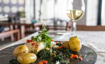 a plate of food with potatoes and other ingredients is displayed next to a glass of white wine at Belmar Spa & Beach Resort