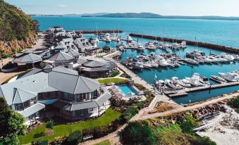 an aerial view of a marina with boats docked , buildings , and a pool , surrounded by mountains at Anchorage Port Stephens
