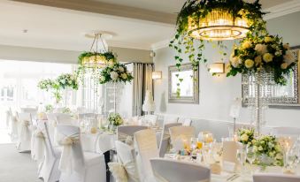 a white dining room with multiple tables set for a wedding reception , each table adorned with white tablecloths and flowers at Harbour Hotel & Spa Christchurch