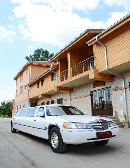a white limousine is parked in front of a building with wooden balconies and trees at Alfa Hotel