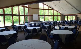 a large room with round tables and chairs , white tablecloths , and a projector screen set up for a gathering at Devil's Head Resort