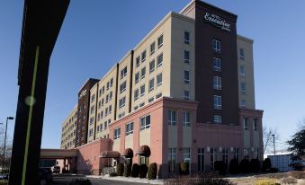 a large hotel with a red and beige facade is shown from the side , with a parking lot in front of it at Hotel Executive Suites