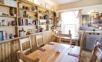 a cozy dining room with wooden tables , chairs , and bookshelves filled with books and vases at The Bell Inn