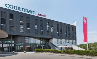 the exterior of the courtyard marriott hotel , a modern , black - and - white design with large windows and balconies , surrounded by trees at Courtyard Basel