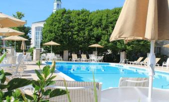 a large outdoor pool surrounded by lounge chairs and umbrellas , with a hotel in the background at Hilton St. Louis Frontenac
