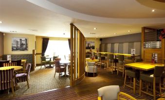 a modern lounge area with yellow chairs and tables , a bar area , and large windows at Premier Inn Burgess Hill