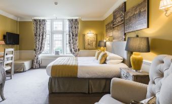 a large bed with white and gold linens is in a room with yellow walls , gray curtains , and two lamps at Coombe Abbey Hotel