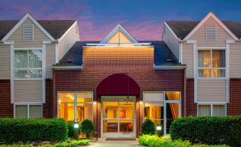 a brick building with a red roof and a large entrance is surrounded by bushes and trees at Sonesta ES Suites Nashville Brentwood