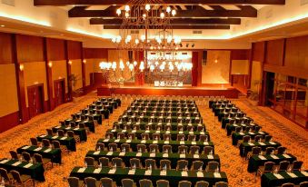 a large conference room with rows of tables and chairs , a chandelier hanging from the ceiling , and a stage at the end at Pelangi Beach Resort & Spa, Langkawi