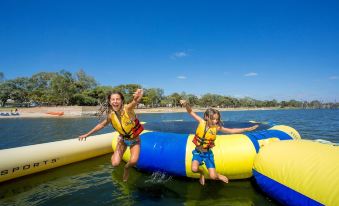 two children are playing on an inflatable raft in a lake , with one of them wearing a life jacket at Discovery Parks - Lake Bonney