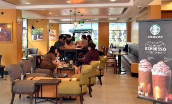 a busy coffee shop with several people seated at tables , enjoying their beverages and snacks at M Hotel