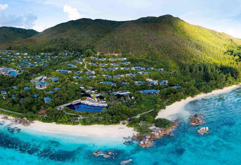 a bird 's eye view of a resort nestled in the mountains with a beach and ocean at Raffles Seychelles