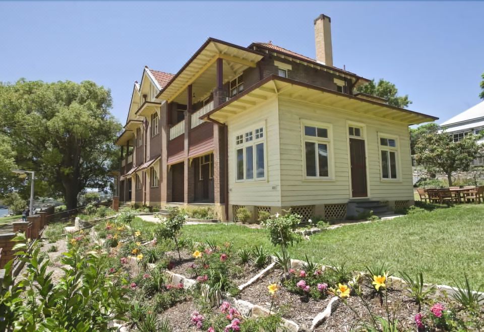 a large , two - story house with a yellow exterior and brown roof is surrounded by greenery and flowers at Cockatoo Island Accommodation