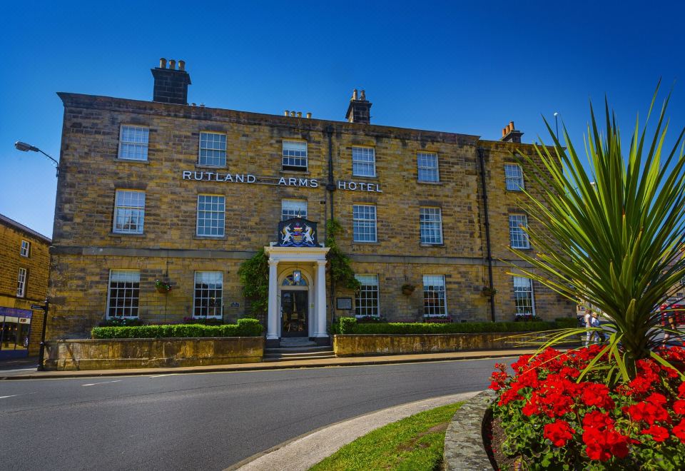 "a large stone building with a sign that says "" rutland arms hotel "" is surrounded by red flowers and greenery" at The Rutland Arms Hotel, Bakewell, Derbyshire
