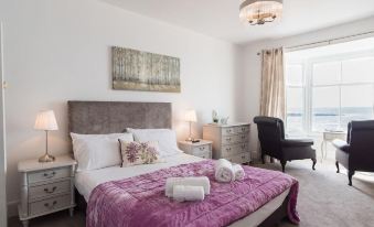 a large bed with a purple blanket and white pillows is in a room with a black chair at Marine Apartment
