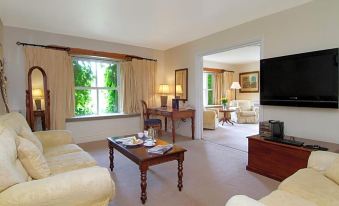 a living room with a couch , coffee table , and television is shown next to a window at BrookLodge & Macreddin Village