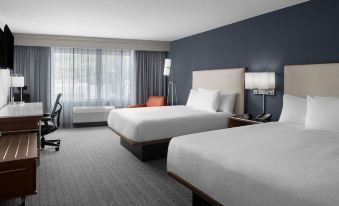 a modern hotel room with two beds , white bedding , and a large window , providing a comfortable and functional atmosphere at Courtyard Los Angeles Burbank Airport