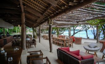 an outdoor dining area with wooden tables and chairs , surrounded by trees and a beach at Island Escape by Burasari
