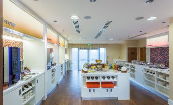 a large kitchen with white cabinets , a wooden floor , and a dining table filled with various food items at Hampton by Hilton Exeter Airport