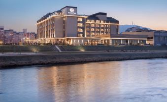 a large hotel building situated on the side of a body of water , with a boat passing by at DoubleTree by Hilton Skopje