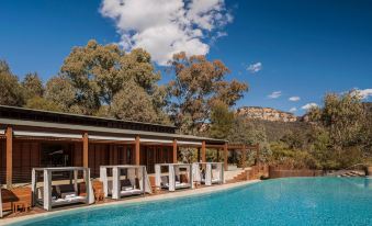 a large swimming pool surrounded by lounge chairs and umbrellas , with a wooden building in the background at Emirates One&Only Wolgan Valley