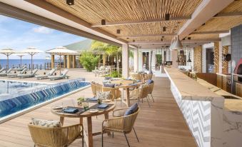 a luxurious outdoor dining area with wooden tables , chairs , and umbrellas , surrounded by a pool and a pool bar at JW Marriott Maldives Resort & Spa