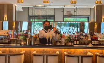 a man wearing a face mask is standing behind a bar , holding a glass of champagne at Hotel Cabo de Hornos