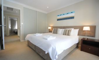 a large bed with white linens and a brown headboard is in a room with a painting on the wall at Mandurah Quay Resort