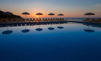 a large outdoor pool with several lounge chairs and umbrellas , reflecting the setting sun over the water at Htop Caleta Palace #HtopBliss