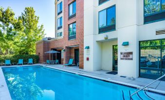 a large swimming pool is in front of a tall , brick building with multiple balconies at SpringHill Suites Athens West