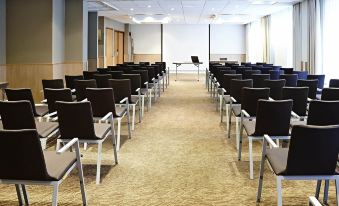 a conference room with rows of black chairs arranged in a semicircle , and a projector screen mounted on the wall at Novotel Leeds Centre