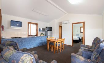 a living room with a blue couch , wooden table , chairs , and a flat - screen tv mounted on the wall at Adelaide Caravan Park - Aspen Holiday Parks