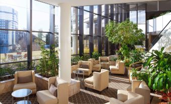 a large , well - lit room with multiple couches and chairs arranged in an open space with greenery and large windows at Hilton Alexandria Mark Center
