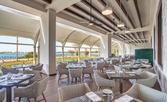a modern restaurant with wooden floors , large windows offering views of the ocean , and various dining tables and chairs at Royalton Negril, An Autograph Collection All-Inclusive Resort