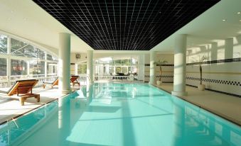 a large indoor swimming pool with white tiles and a black ceiling , surrounded by lounge chairs at Hiroshima Airport Hotel