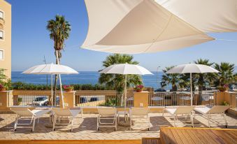 a beach scene with several lounge chairs and umbrellas set up on a wooden deck at Hotel Punta Nord Est