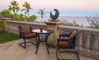 a patio with a table and two chairs , surrounded by palm trees and overlooking the ocean at Villa del Faro