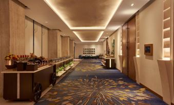 a long hallway with a blue and gold carpet , featuring rows of potted plants on the floor at Courtyard by Marriott Mumbai International Airport