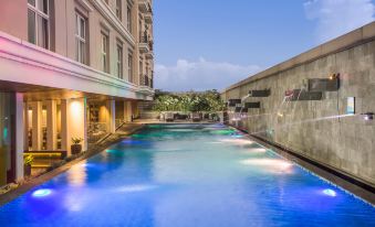 a long , narrow pool with blue water is surrounded by a building and has a few trees in the background at Swiss-Belhotel Bogor