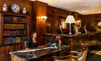 two women are sitting at a reception desk in a hotel lobby , surrounded by books at The Townsend Hotel