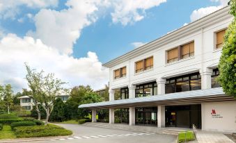 a modern , white building with large windows and a sloping roof , surrounded by trees and a parking lot at Izu Marriott Hotel Shuzenji