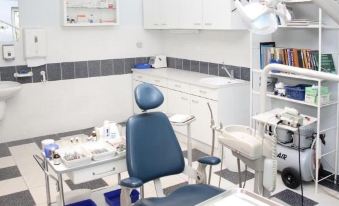 a dental office with a blue chair in the center of the room , surrounded by various dental tools and equipment at Hotel Arboretum