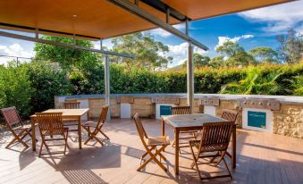 an outdoor dining area with wooden tables and chairs , surrounded by a lush green garden at Ingenia Holidays Lake Conjola