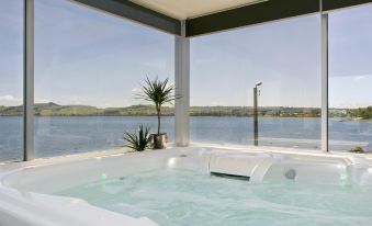 a hot tub with a large window overlooking a body of water , creating a serene and relaxing atmosphere at The Cove