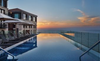 a large swimming pool with a modern building and lounge chairs is seen at sunset at The Setai Tel Aviv, a Member of the Leading Hotels of the World
